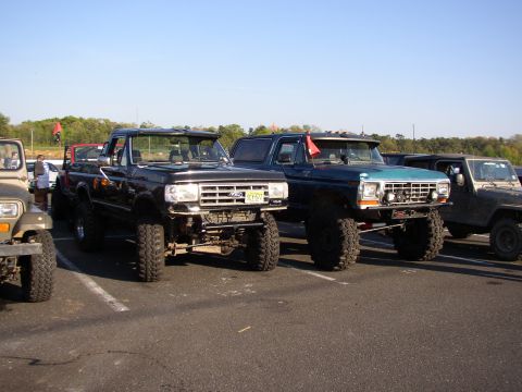 1995 Ford Bronco - Two lifted Ford trucks and a Jeep parked side-by-side at an outdoor event.
