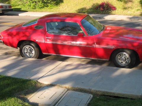 1986 Ford Bronco - A red coupe, likely from the 1970s, is parked on a residential street with a flat rear tire.