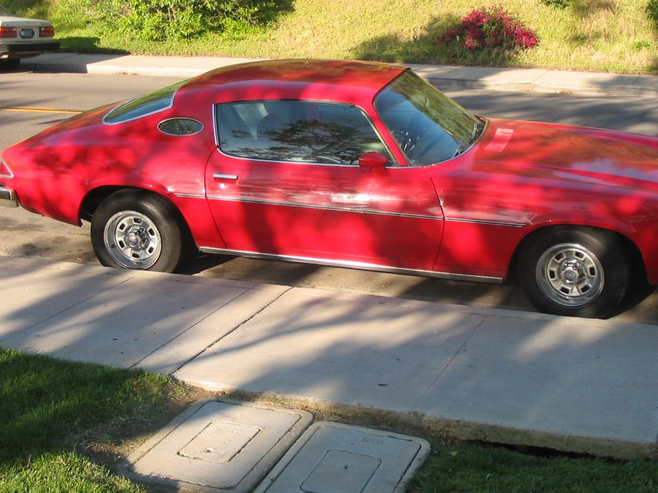 Red coupe with a flat rear tire parked on a sidewalk. Chrome trim along the bottom