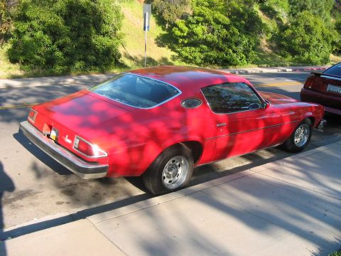 1986 Ford Bronco - A red coupe from the 1970s is parked on the street next to a sidewalk.