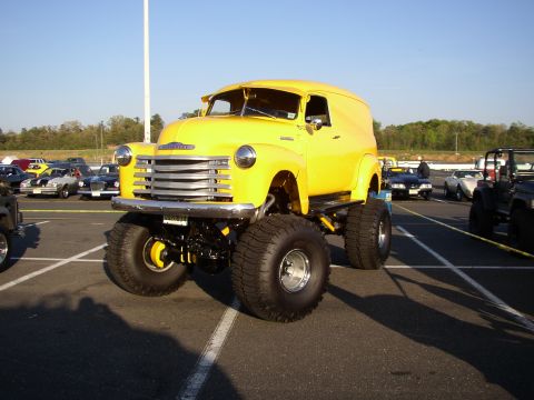 1995 Ford Bronco - A bright yellow panel van, likely from the 1950s, is prominently displayed with a lifted chassis and oversized tires at a car show.