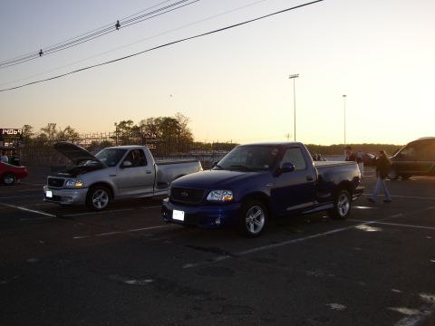 1995 Ford Bronco - Two Ford pickup trucks, a blue Lightning and a silver F-150, are parked at an outdoor event.