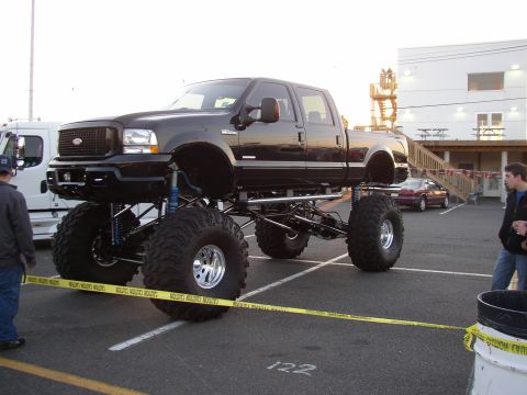 1995 Ford Bronco - A heavily modified black Ford pickup truck with extreme lift and oversized tires is parked in a lot.