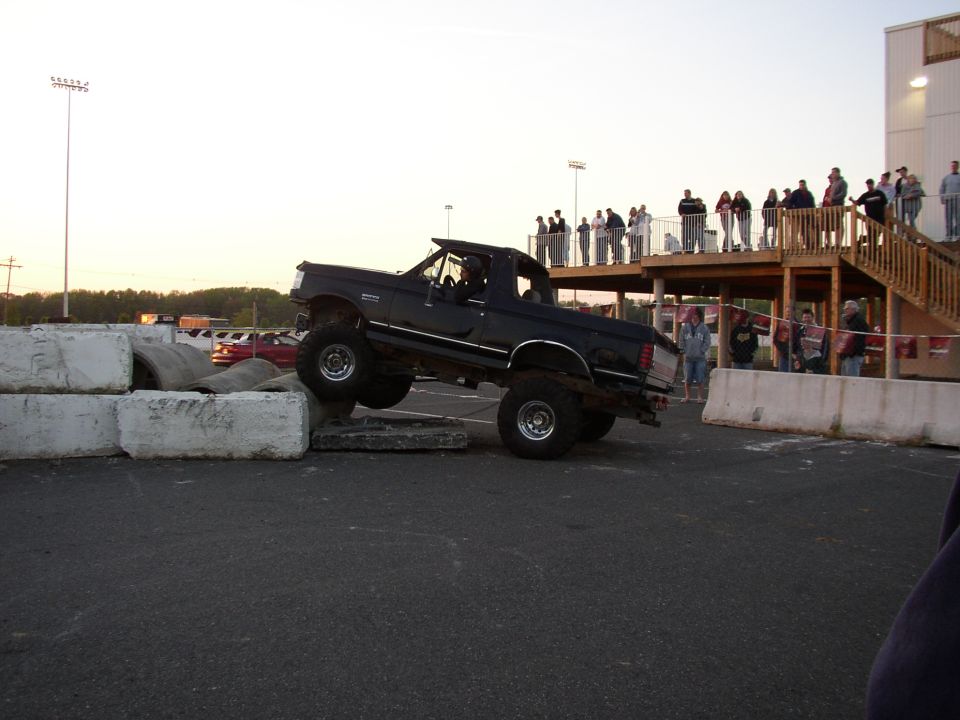 Lifted black pickup truck driving over concrete barriers with people watching from a deck