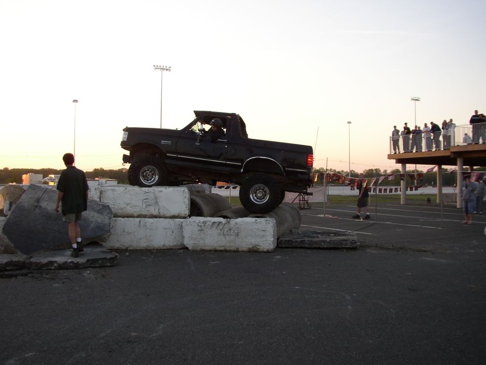 Black 1995 Ford Bronco on concrete blocks, driver visible, off-road course