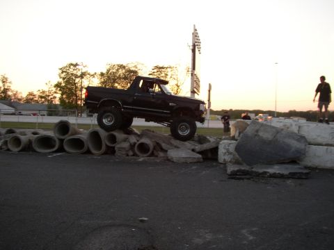 1995 Ford Bronco - A lifted black truck navigates an obstacle course made of concrete pipes and large rocks.