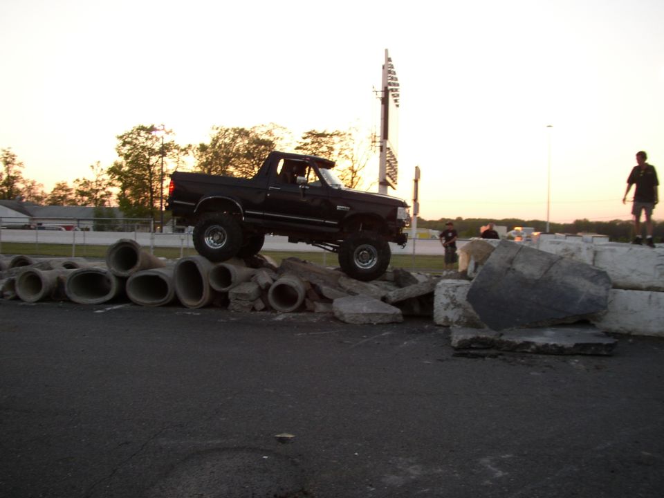 Black lifted truck with large tires driving over concrete pipes and rocks