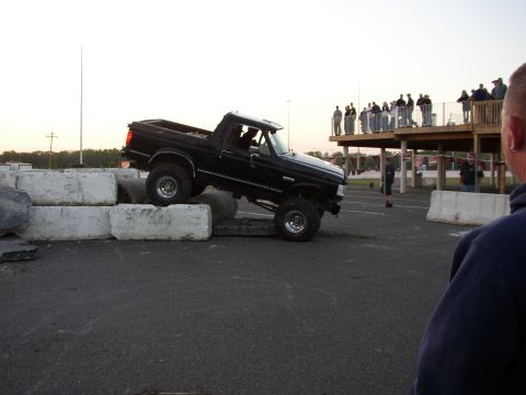 1995 Ford Bronco - Lifted pickup truck navigates an obstacle course with onlookers watching from a raised deck.
