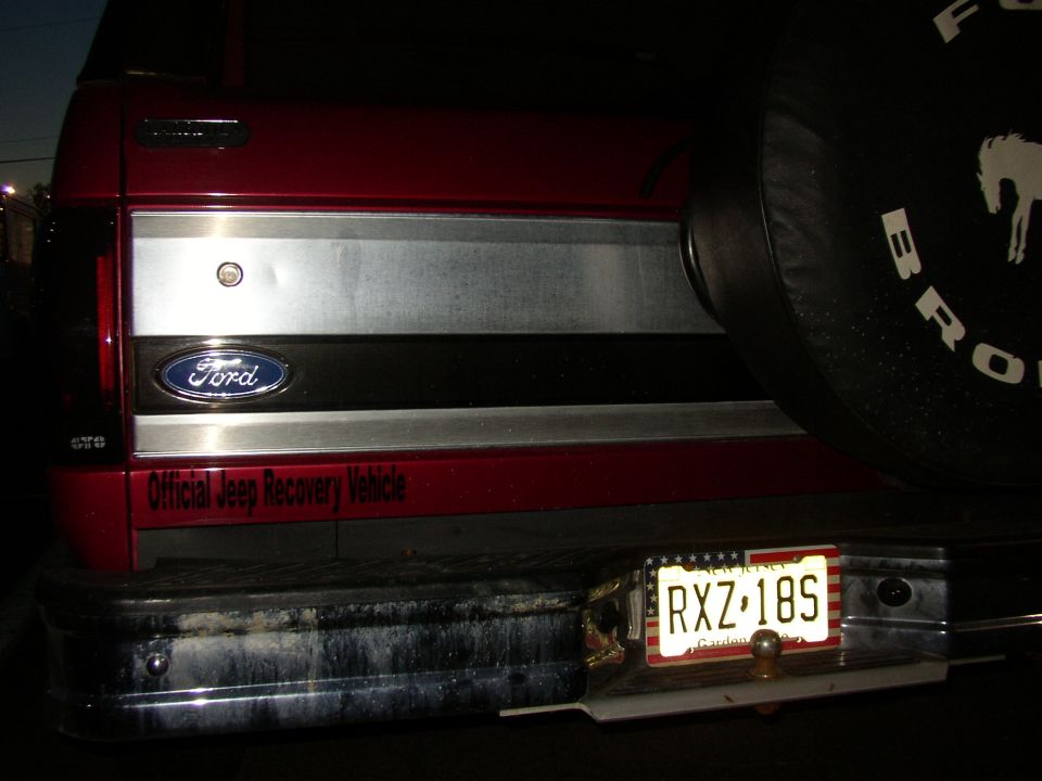 Rear of red Ford Bronco at night with Bronco spare cover, ball hitch and NJ plate