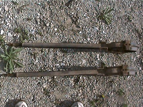 1977 Ford F-150 - Two truck axles are shown resting on a gravel surface with some weeds growing around them.
