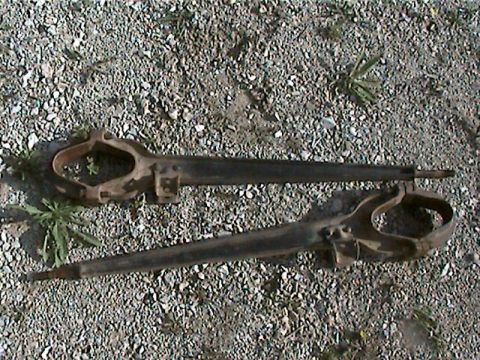 1977 Ford F-150 - Two rusty metal suspension components are shown on a gravel surface.