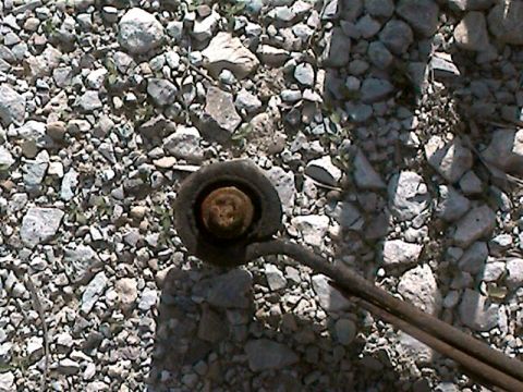 1977 Ford F-150 - A close-up view of a leaf spring bushing resting on a gravel surface, with the Supermotors.net logo in the lower right corner.