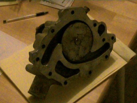 1977 Ford F-150 - A close-up view of a metal water pump, likely for a vehicle, rests on a surface with a pen and papers.