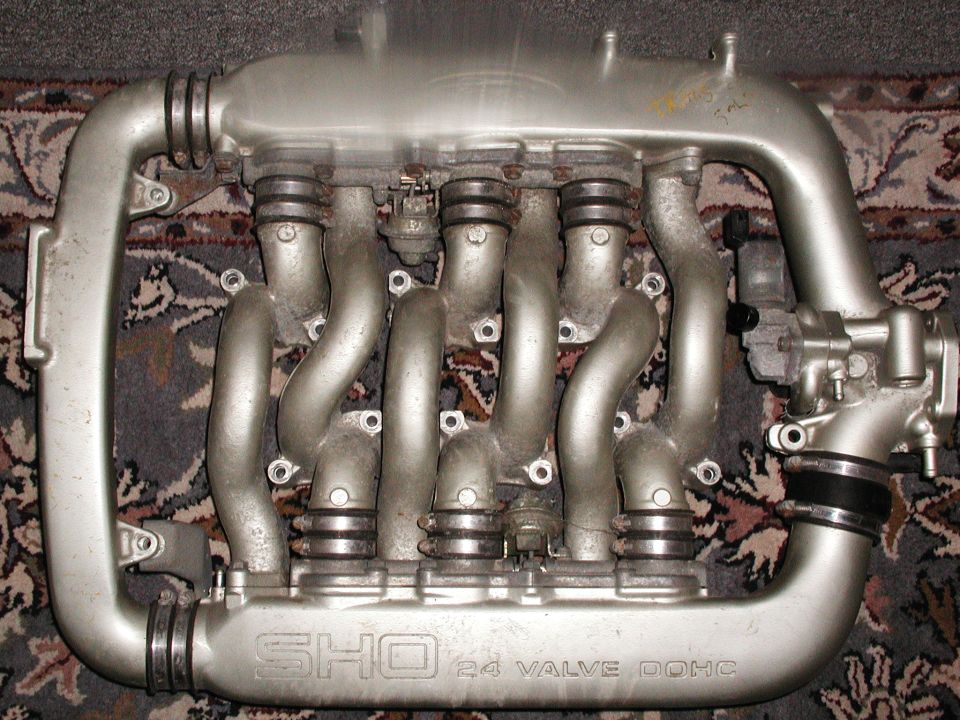 Aluminum intake manifold with curved runners marked SHO 24 VALVE on a patterned rug