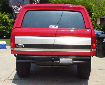 1990 Ford Bronco - Rear view of a red full-size Ford Bronco with a hardtop and chrome trim band parked in a backyard driveway near a basketball hoop.