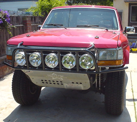 1990 Ford Bronco - Front view of a red Ford Bronco fitted with a tubular prerunner bumper, five round driving lights, and a skid plate.