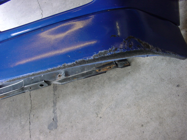 Blue bumper with rust and damage, showing metal support structure