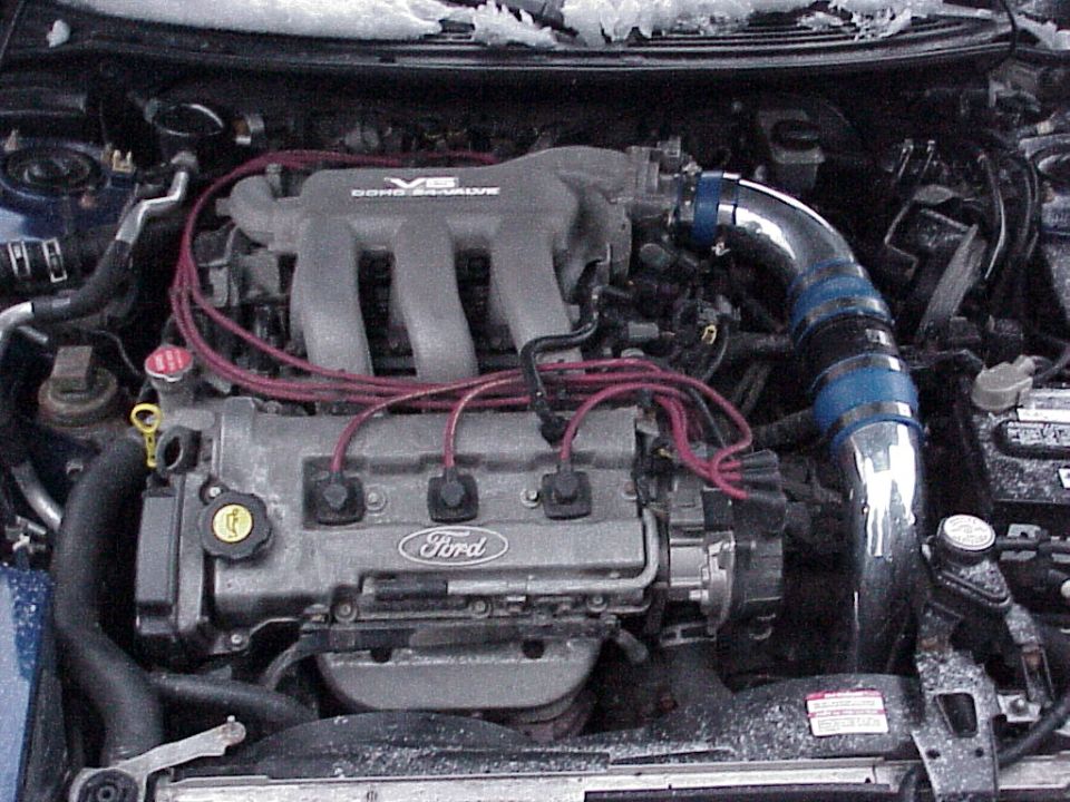 Ford V6 DOHC 24-valve engine bay with red plug wires and chrome aftermarket intake with blue couplers