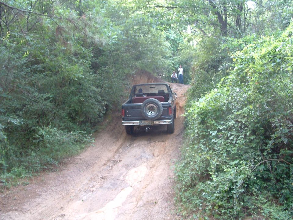 Dark colored 1993 Ford Bronco with a spare tire mounted on the rear, driving up a dirt path