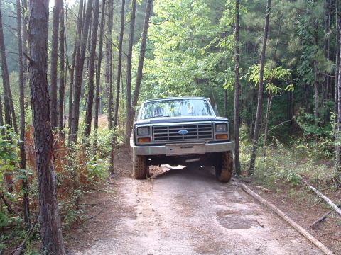 1993 Ford Bronco - A Ford truck navigates a wooded trail, its front grille clearly visible.