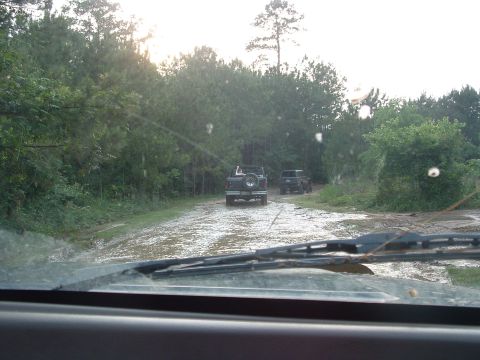 1993 Ford Bronco - Two SUVs navigate a muddy road through a wooded area.