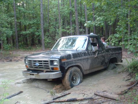 1993 Ford Bronco - This black Ford truck is stuck in a muddy wooded area, with its front wheel deep in the mire.