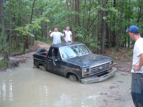 1993 Ford Bronco - Ford Bronco stuck in mud pit with people on top and watching.