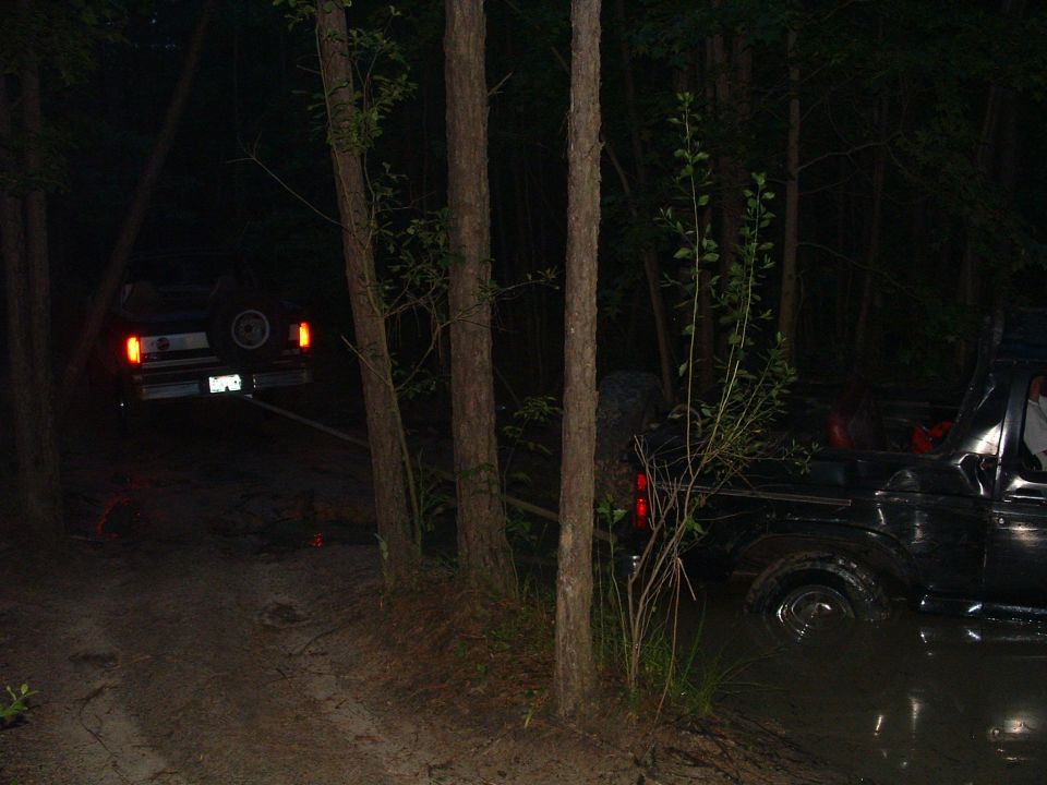 Two black SUVs stuck in mud at night, one being towed