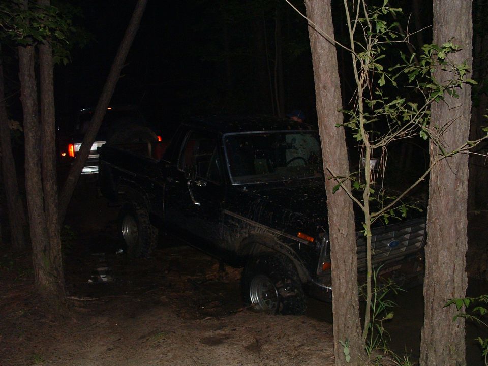 Black Ford Bronco stuck in mud off-road at night, another vehicle visible in background