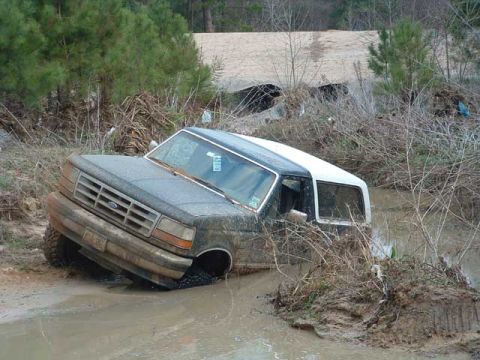 1993 Ford Bronco - A gray Ford Bronco is stuck in muddy water, with its front end partially submerged and surrounded by debris.