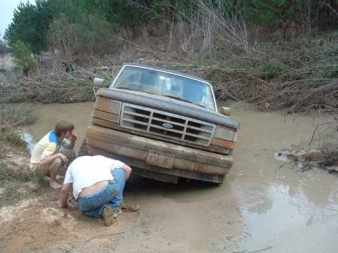 1993 Ford Bronco - A 1993 Ford Bronco is stuck in a muddy ditch with two people assessing the situation.