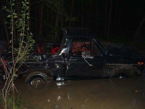 1993 Ford Bronco - This black Ford Bronco is submerged in mud and water, with only the top half visible.