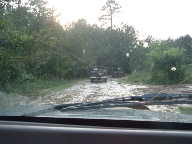 1993 Ford Bronco driving on a muddy road with another SUV behind it