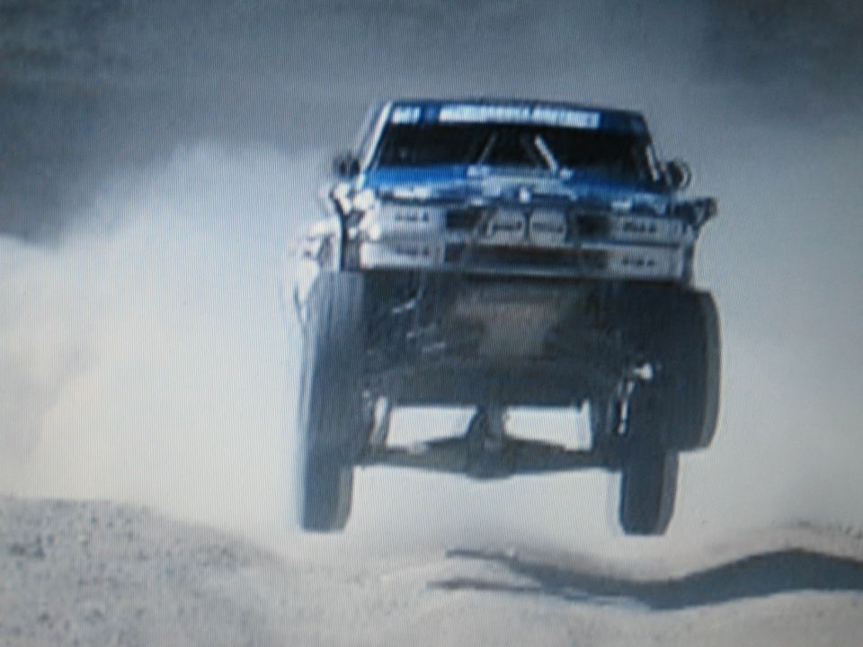 Blue off-road race truck airborne front-on in a dust cloud