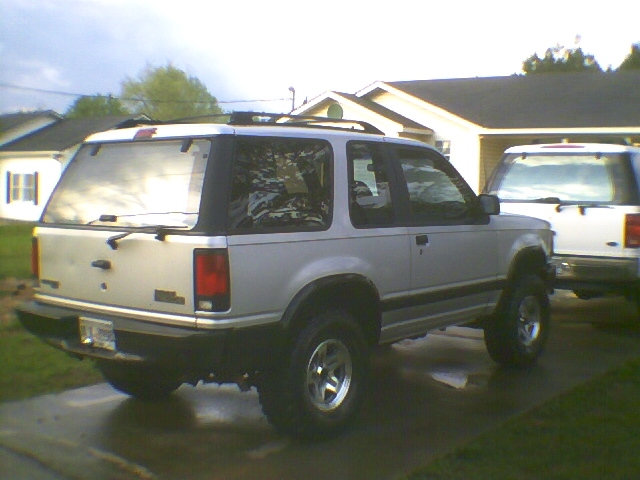 White two-door lifted SUV, rear 3/4 view, parked in driveway by house