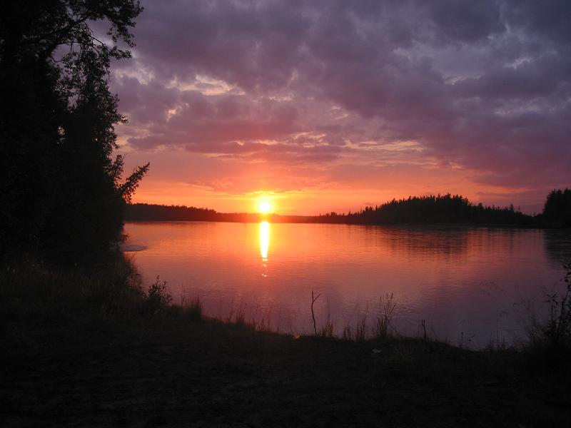 Orange sunset reflecting on calm water with silhouetted spruce treeline