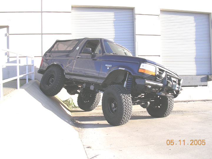 Lifted dark blue Ford Bronco flexing suspension on a concrete ramp by a loading dock