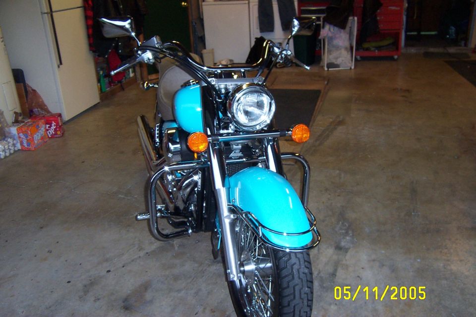 Front view of a turquoise cruiser motorcycle with chrome fender trim and spoke wheel in a garage