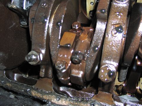 1979 Ford Bronco - Close-up looking up into the bottom end of an engine with the oil pan removed, showing oil-coated crankshaft counterweights, main bearing c…