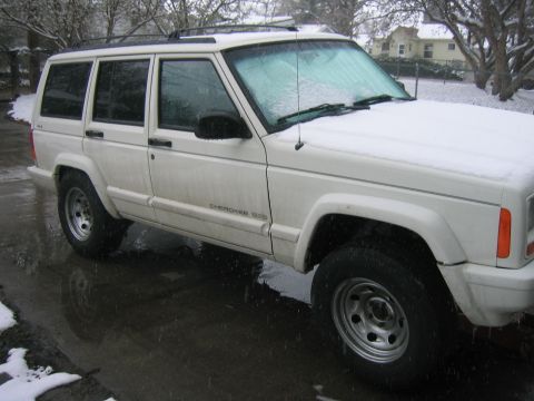 1997 Jeep Cherokee - A white 1997 Jeep Cherokee 4-door SUV is parked on a wet road with snow on the ground and on the vehicle.