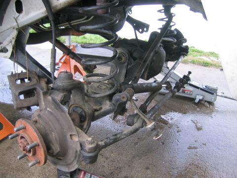 1997 Jeep Cherokee - The front suspension and brake components of a vehicle are shown, supported by jack stands and a hydraulic jack.