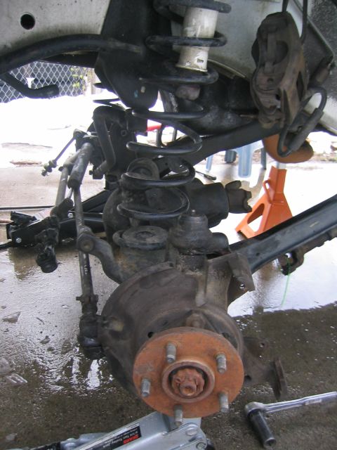 1997 Jeep Cherokee - Close-up of a vehicle's front suspension and brake assembly, showing rusty components and coil springs.