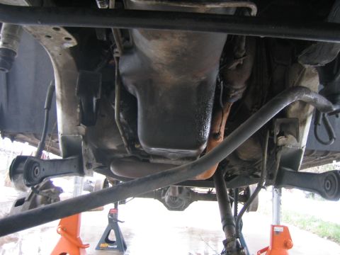 1997 Jeep Cherokee - The underside of a vehicle is shown, supported by jack stands, with a focus on the engine's oil pan and suspension system.