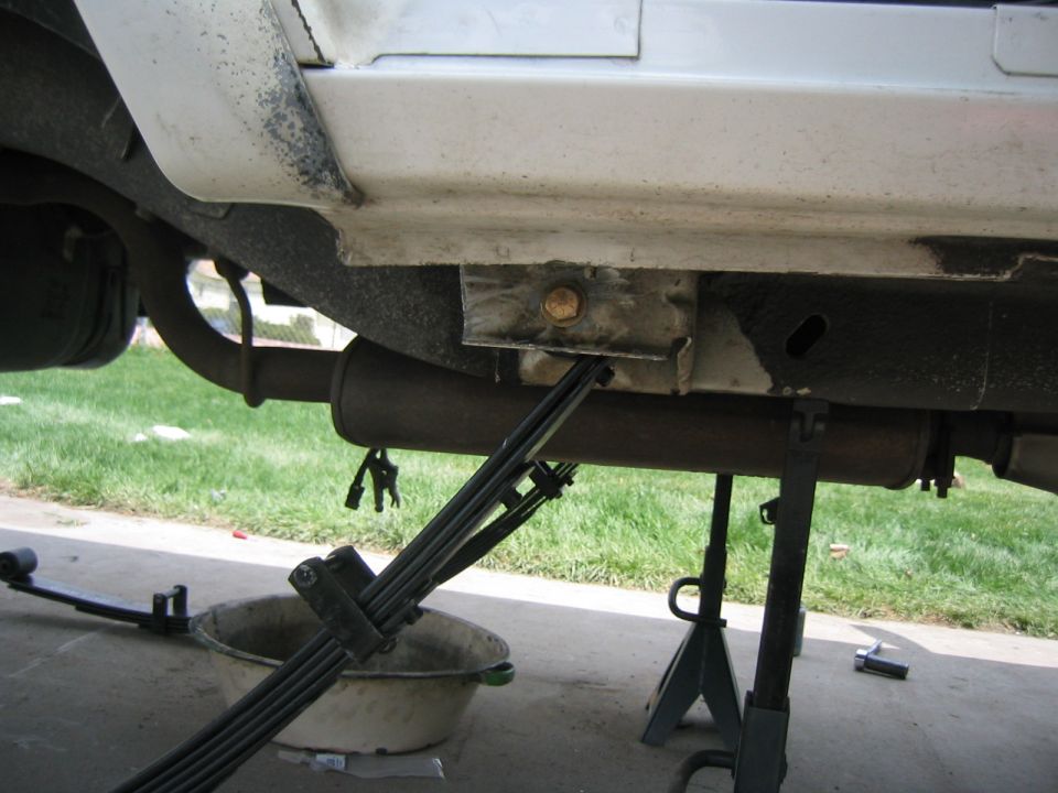 Underbody view of a white vehicle's leaf springs and exhaust system