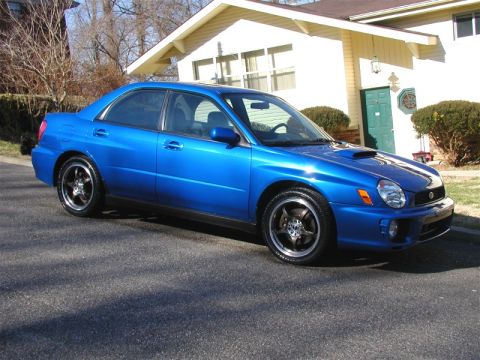 2002 Subaru Impreza - A blue Subaru Impreza sedan is parked on a street in front of a residential house.