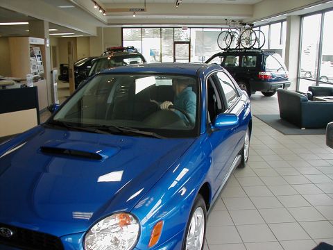 2002 Subaru Impreza - A blue 2002 Subaru Impreza WRX is displayed in a dealership showroom with other vehicles visible in the background.
