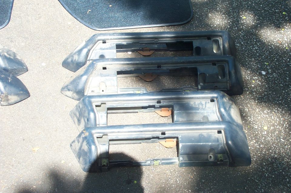 Three dark gray car bumper sections stacked on asphalt