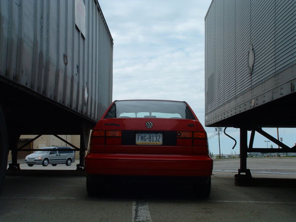 Red Volkswagen Jetta rear view between two trailers. License plate reads FMG-8132