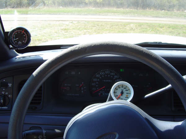 Dashboard gauges in a 1998 Ford Crown Victoria, showing speedometer and aftermarket gauges