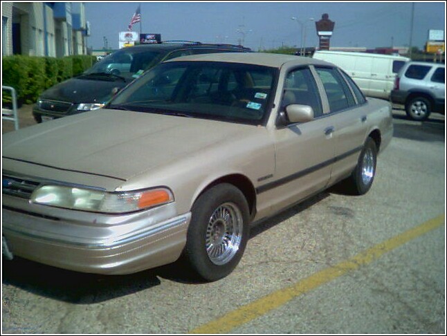 Tan Ford Crown Victoria sedan parked in a lot, front three-quarter view